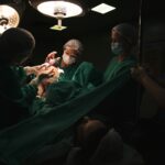 Doctors and nurses delivering a newborn baby under surgical lights in a hospital.