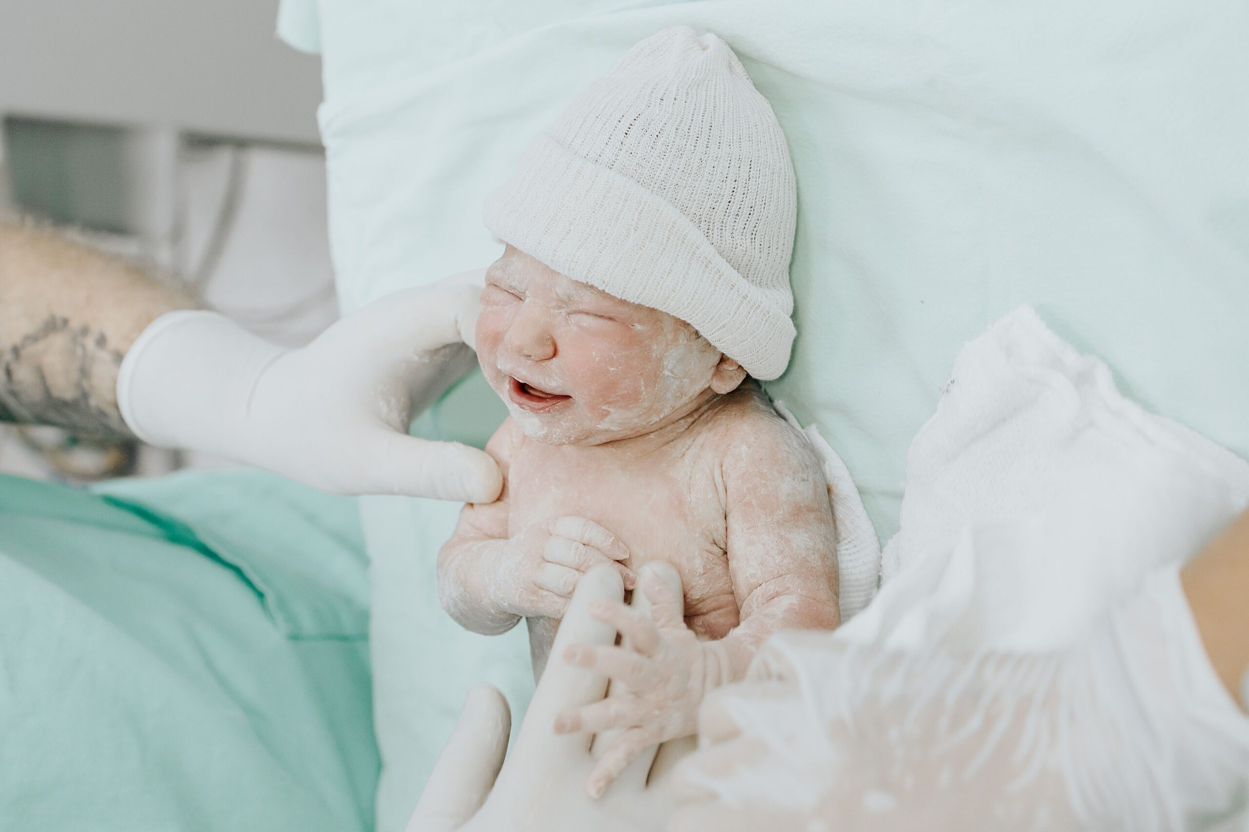 A newborn baby just delivered, attended by medical staff wearing gloves in a hospital setting.