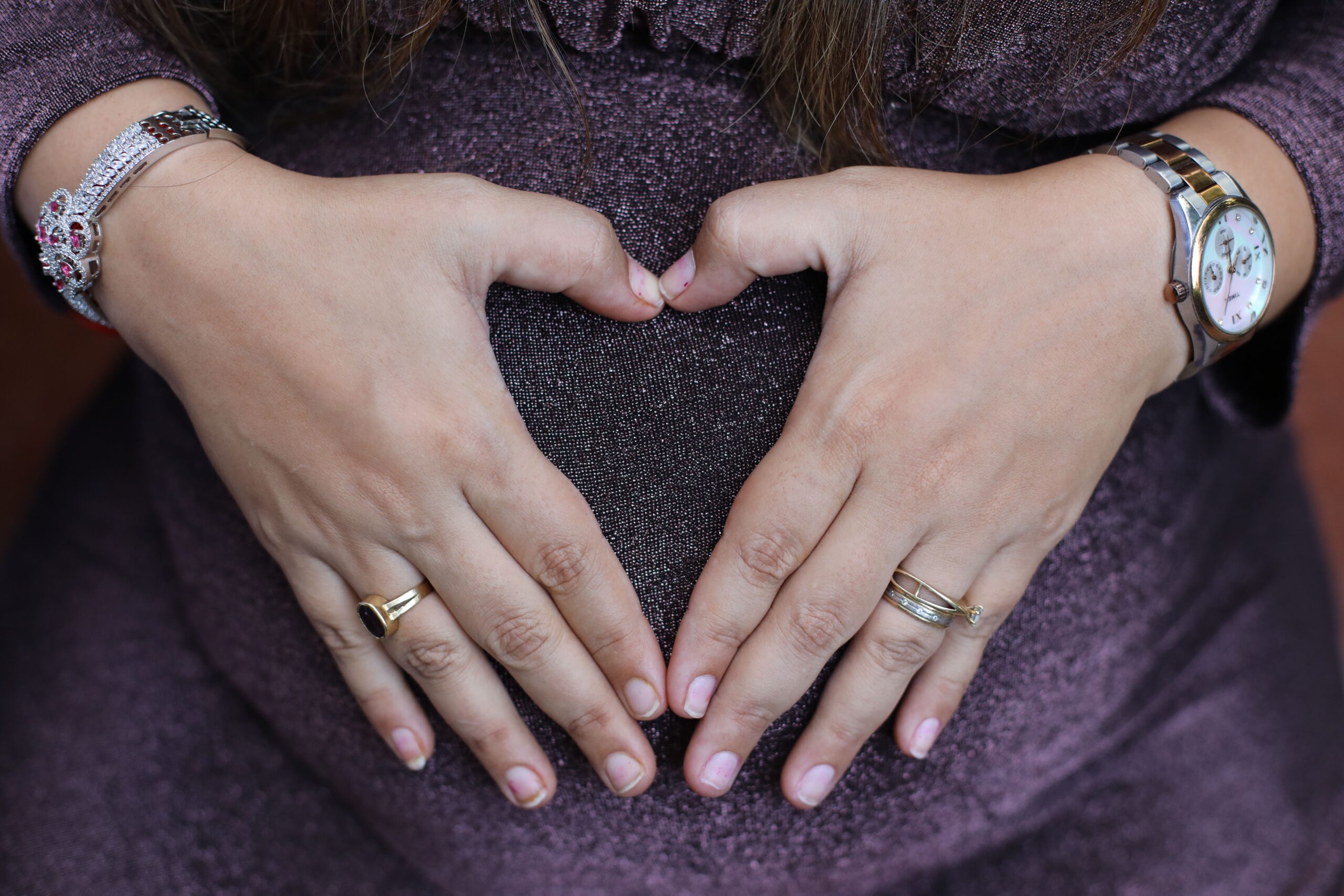 Close-up of pregnant woman creating heart shape on belly as a loving gesture.