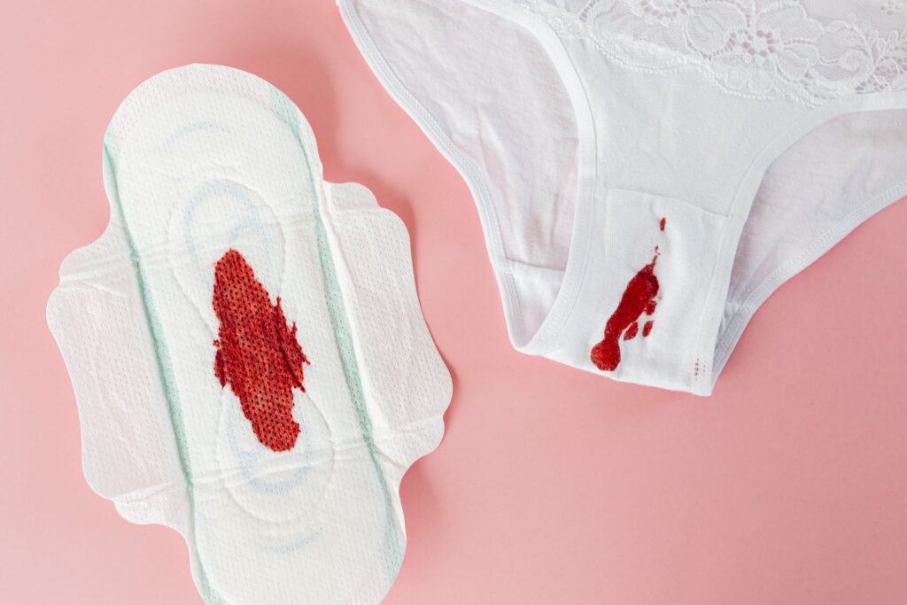 Close-up of white panty and sanitary pad with menstrual blood on pink background.
