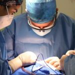 Surgeons in operation room wearing masks and gloves performing surgery.