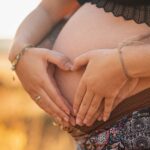 Close-up of a couple's hands forming a heart over a pregnant belly, symbolizing love and family.