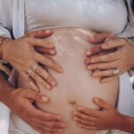 Hands of family members lovingly touching a pregnant belly outdoors, symbolizing unity and new beginnings.