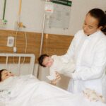 A doctor assists a new mother with her newborn baby in a hospital room setting.