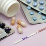 Image featuring a pregnancy test strip surrounded by various pills and capsules on a pastel background.
