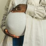 Pregnant woman in casual attire gently holding her belly, symbolizing motherhood.