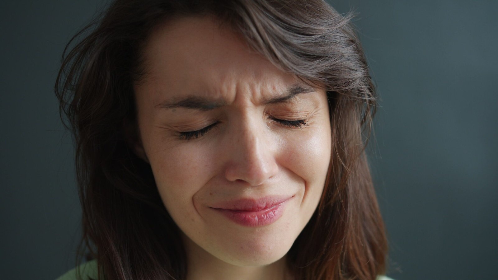 Close-up of a woman expressing emotion with eyes closed and a frown.