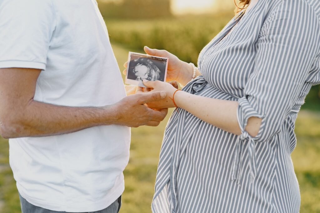A couple holds an ultrasound image, representing pregnancy and family love, in an outdoor setting.