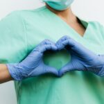 Nurse in blue gloves making a heart shape with hands, symbolizing compassion and care.