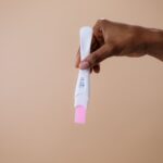A woman's hand holding a positive pregnancy test on a neutral background.