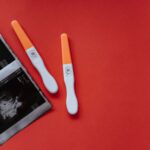 A flat lay of two pregnancy tests and ultrasound images on a red background, conveying anticipation and excitement.