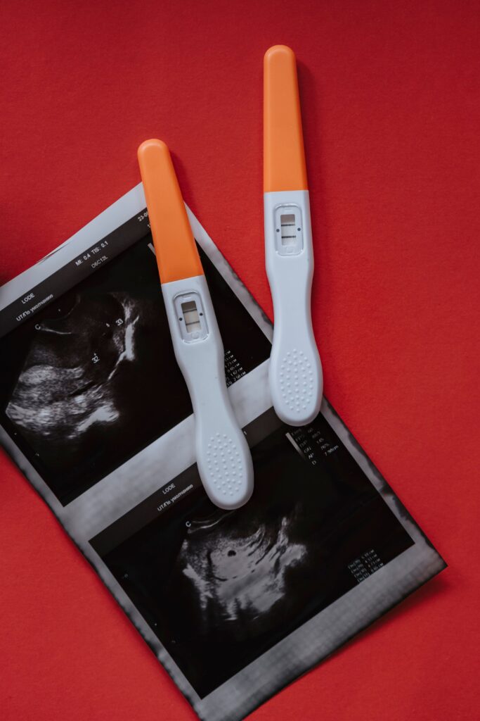 Two pregnancy tests and an ultrasound image on a red surface, indicating positive results.