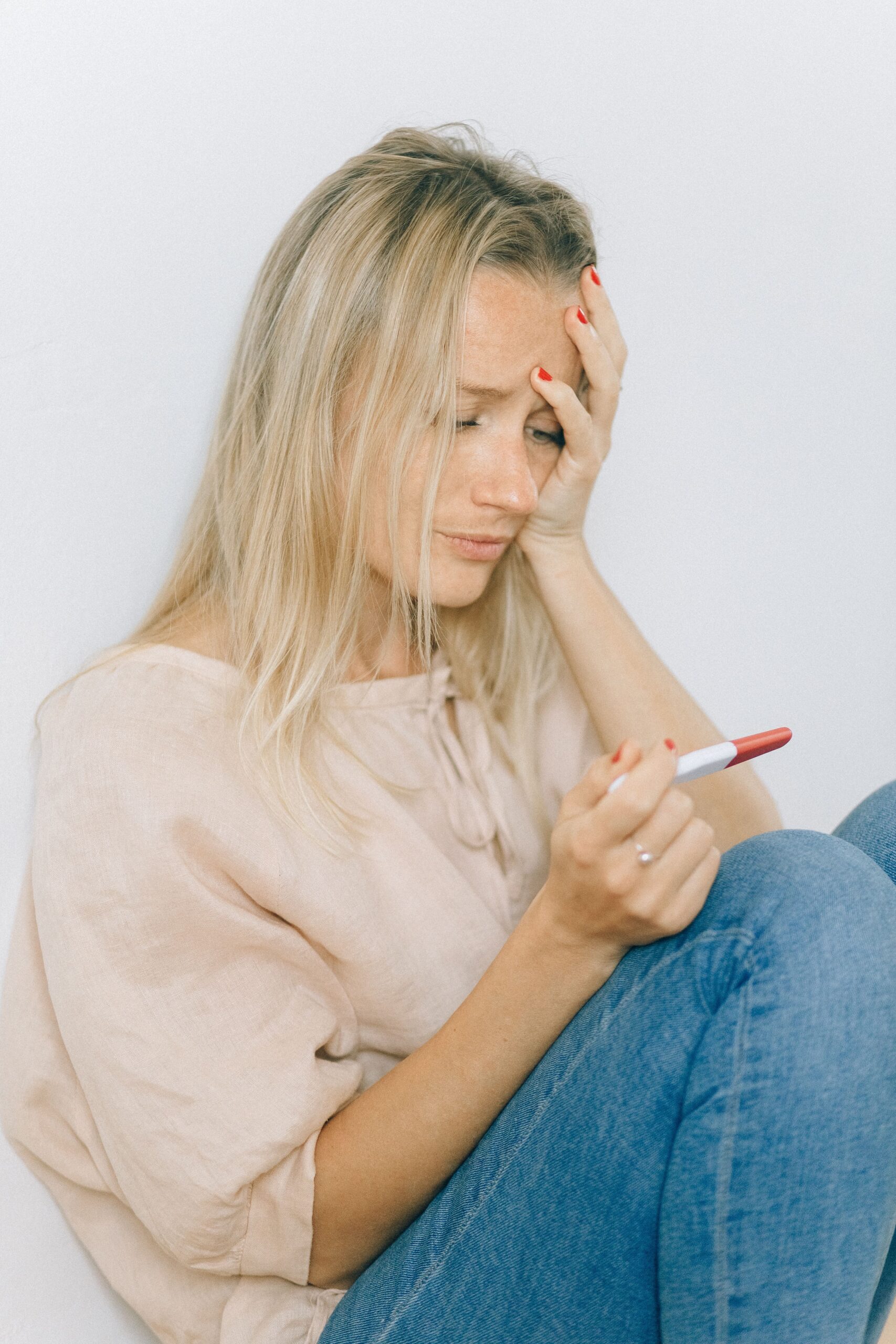 A worried woman sitting indoors holding a pregnancy test, expressing uncertainty.