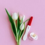 Flat lay of pregnancy test, pacifier, and tulips on pink surface conveying fertility and new beginnings.