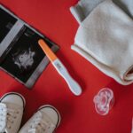 Flat lay of baby essentials with pregnancy test and ultrasound on red background.
