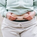 Crop anonymous plus sized female in casual hoodie touching and showing fat on belly while standing in park