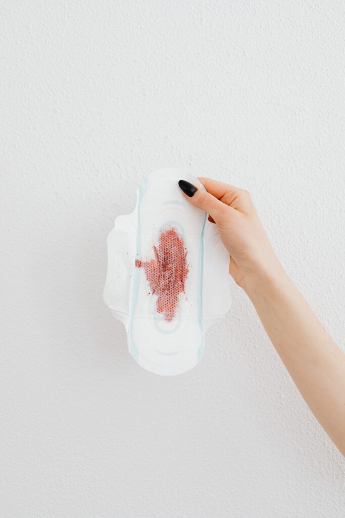 A hand is holding a blood-stained sanitary pad on a light background, highlighting menstruation.