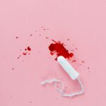 White tampon with red blood stain on pink surface. Menstrual health concept.