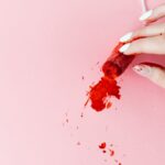 A close-up of a hand holding a tampon with blood on a pink background, symbolizing menstruation and menstrual health.