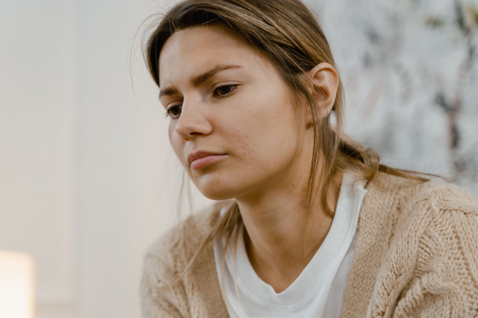 A woman wearing a cardigan appears thoughtful and introspective indoors.